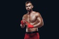 Muscular young fighter is applying bondage tape on hands getting ready to fight isolated on black background