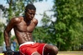 Muscular young man exercising at the sports field. African man looking to the side while doing horizontal bar exercises