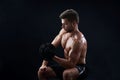 Muscular young man lifting weights on black background