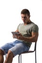 Muscular young man sitting on chair while reading from e-book device Royalty Free Stock Photo