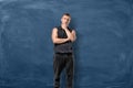 Muscular young man is standing and thinking holding his head with hand on blue chalkboard background Royalty Free Stock Photo