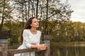 Dreaming pensive young woman stands leaning on a railing of a wooden bridge in a white dress looking forward Royalty Free Stock Photo