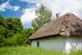 Rural landscape with whitewashed, thatch roof cottage, a grassy meadow, trees and blue, cloudy sky Royalty Free Stock Photo