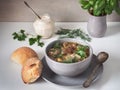 Mushroom soup in a deep gray ceramic plate. Bread rolls and fresh basil in a clay pot on a white table Royalty Free Stock Photo