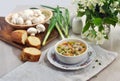 Mushroom soup in a small white bowl. Fresh bread, champignons, green onions on a white table.