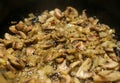 Mushrooms and onion sliced cooking on a black hot frying pan.