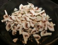 Mushrooms and onion sliced cooking on a black hot frying pan.