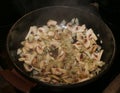 Mushrooms and onion sliced cooking on a black hot frying pan.