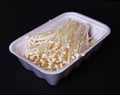 Mushrooms in white container over black background, enoki