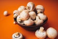 Mushrooms in a wooden bowl on an orange background. The small white champignon in a plate and scattered near it. Royalty Free Stock Photo