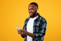 African Man Using Phone Wearing Earbuds Standing Over Yellow Background Royalty Free Stock Photo