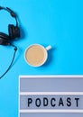 Music background with Podcast word on lightbox, headphones and cup of coffee on blue table, flat lay. Top view, flat lay, space