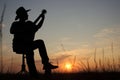 Music concept of black silhouette of man with western hat cowboy and instrument with grass at sunset or sunrise. Musician play