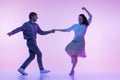 Dynamic portrait of young dancers, man and woman in vintage style outfits dancing swing isolated on lilac color