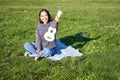 Music and instruments. Portrait of cute asian girl shows her white ukulele, plays in park while sitting relaxed on Royalty Free Stock Photo