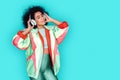 Music lover. Mulatto girl in colorful jacket and headphones standing isolated on blue listening music closed eyes joyful Royalty Free Stock Photo