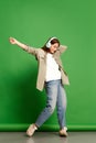 Portrait of young girl, teenager wearing wireless headphones dancing and listening to music with joy over green Royalty Free Stock Photo