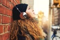 Music is my escape. a young woman listening to music while leaning against a brick wall outside.