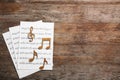 Music notes with sheets on wooden background, flat lay. Royalty Free Stock Photo