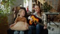 A woman energetically plays the guitar and sings cheerfully with a girl