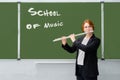 A music teacher plays the flute. Learning to play wind musical instruments against a blackboard with the text