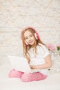 Music and technology. Portrait of young girl in pajamas with white laptop and wireless pink headphones on background