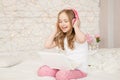 Music and technology. Portrait of young girl in pajamas with white laptop and wireless pink headphones, sing song on