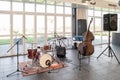 Musical instruments, double bass next to a drums, speakers and microphones inside a room on a sunny day.