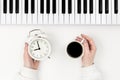 Musical keyboard, alarm clock and a cup of coffee in female hands, top view.