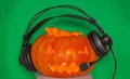Pumpkin on a green plain background for Halloween with glowing eyes nose and mouth listening to the radio