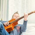 Musical young boy strummin on a guitar at home