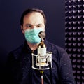 A musician in a medical mask sings at a microphone in a black-walled recording studio