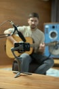 Musician playing acoustic guitar, records song on phone, shooting online lesson for social network. Guy out of focus