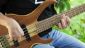 The musician plays a five-string bass guitar with his fingers on the street in the summer