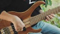 The musician plays a five-string bass guitar with his fingers on the street in the summer