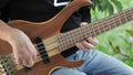 The musician plays a five-string bass guitar with his fingers on the street in the summer