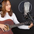 Musician producing music in professional recording studio. Young asian woman with headphone sing while playing an acoustic guitar Royalty Free Stock Photo