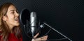 Musician producing music in professional recording studio. Young asian woman in red t-shirt singing in front of black soundproof Royalty Free Stock Photo