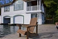 A Muskoka chair sitting on a wood dock facing a calm lake. Pier for boat and balcony for a vista of the lake