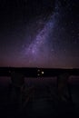 Muskoka chairs on a dock at night with the Milky Way in the background.