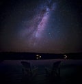 Muskoka chairs on a dock at night with the Milky Way in the background.