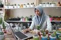 A Muslim businesswoman is selling succulent plants on internet. She has a clean and white workshop.