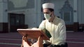 Muslim cleric reading quran with mask