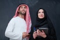 Muslim couple using modern technology in front of black chalkboard