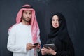 Muslim couple using modern technology in front of black chalkboard