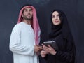 Muslim couple using modern technology in front of black chalkboard