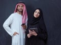 Muslim couple using modern technology in front of black chalkboard