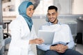 Muslim Dentist Lady Holding Digital Tablet, Showing Treatment Plan To Male Patient