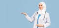 Muslim doctor or nurse woman in a hijab with a stethoscope in a white coat shows with her hand to the space for text. on a blue
