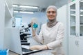 Muslim female chemistry student in hijab sitting at a table in a research laboratory and studying liquid substances Royalty Free Stock Photo